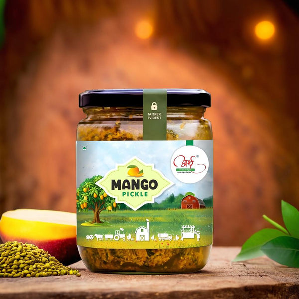 A jar of homemade mango pickle with a label featuring an illustration of a tree and text, alongside raw mangoes and spices visible.