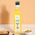 A clear glass bottle of Arth Agro Farms Wood-Pressed Groundnut Oil with a label showing the brand logo and product name, accompanied by a small bowl of peanuts and a wooden bowl with groundnut shells on a white surface against a beige background.