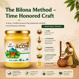 A jar of A2 Desi Cow Ghee with an illustration of a woman using a traditional ghee churner, set against a beige background with green leaves.